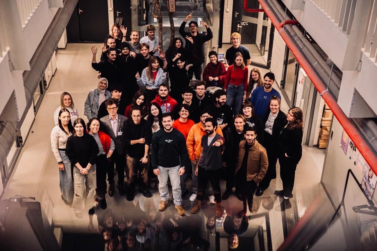 Winter School participants waving up at the camera from the floor of an atrium at VILNIUS TECH