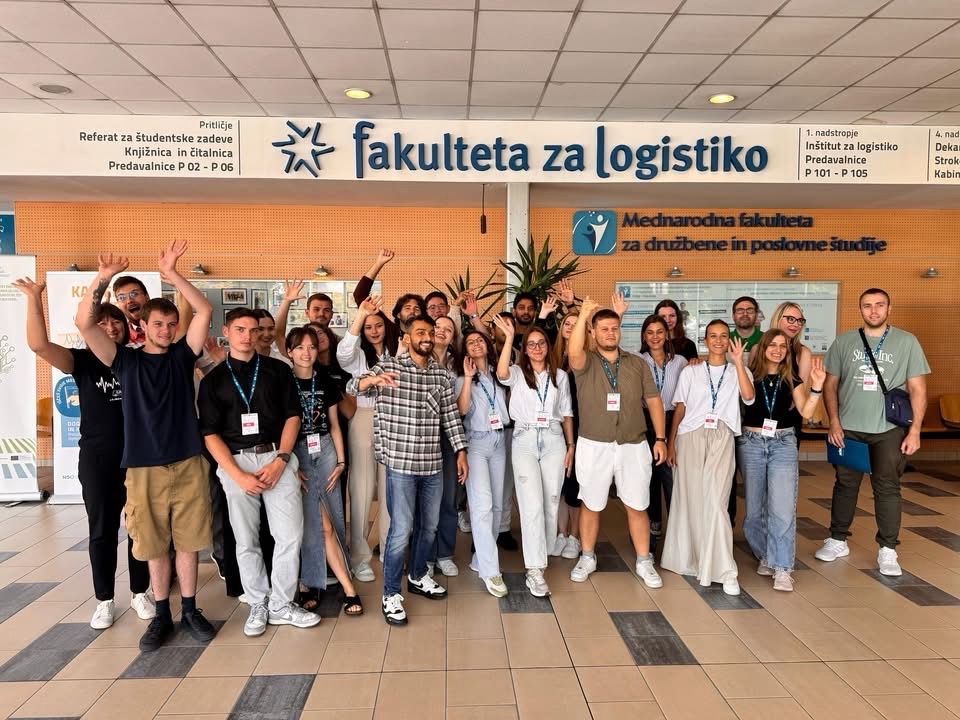 A large group of summer school participants waving in the entrance hall of the Faculty of Logistics
